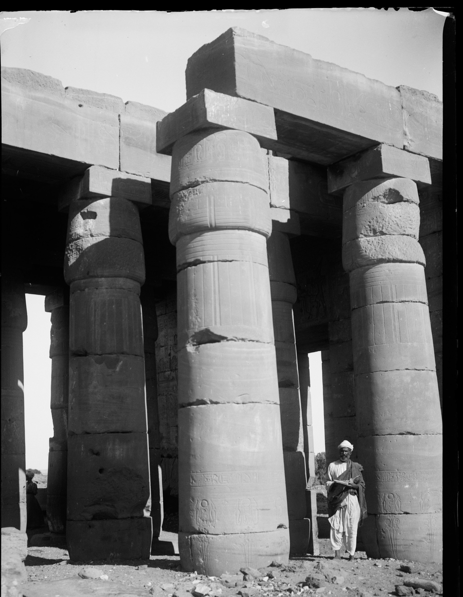 "Rameseum. " (Bildetekst fra album) En mann av lokal befolkning mellom høye tempelsøyler.