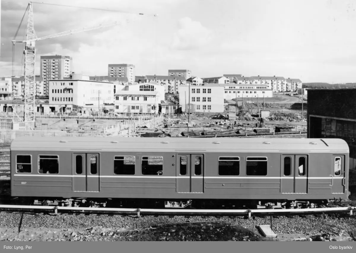 Oslo Sporveier. T-banevogn 1007, serie T1 (fra 1964-1965), foran Ryen vognhall, typebilde. Verkstedet bygges i bakgrunnen. Heisekran. Blokkbebyggelse på Manglerud i bakgrunnen.