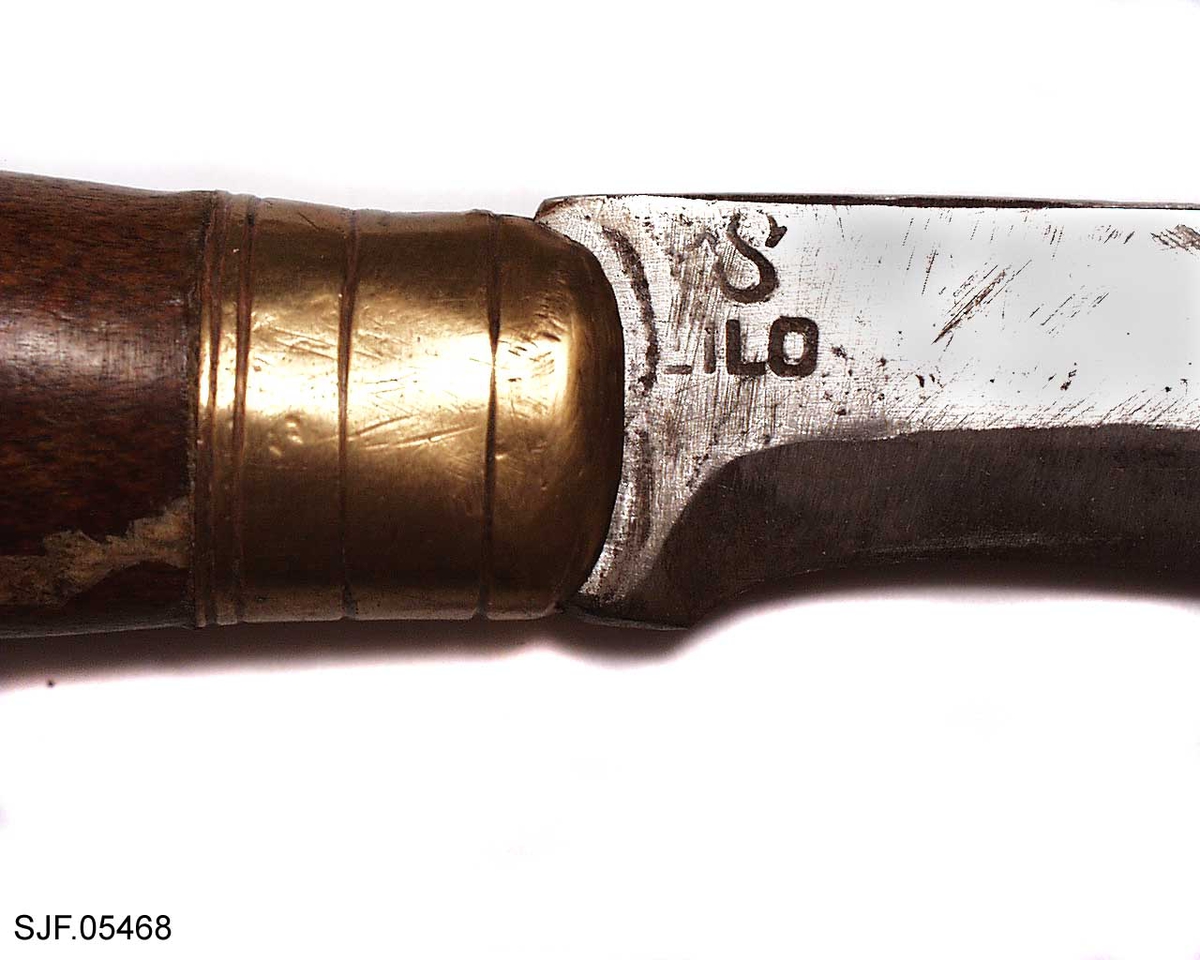 Kniven har brunbeiset skaft, antageligvis av bjørk. Slire og holker er av messing. Slira er foret med papp. Hempa er av imitert krokodilleskinn. Kniven er innkjøpt sammen med andre kniver i ei samling fra Birger Arntzen. 
