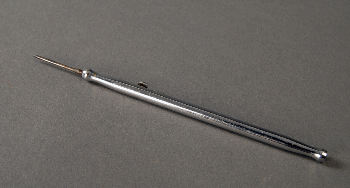 Et lite metallrør som fungerer som en holder for en lansett og en korneaskrape. En skyvbar knott på sylinderen/røret brukes til å få frem lansetten og skrapen.