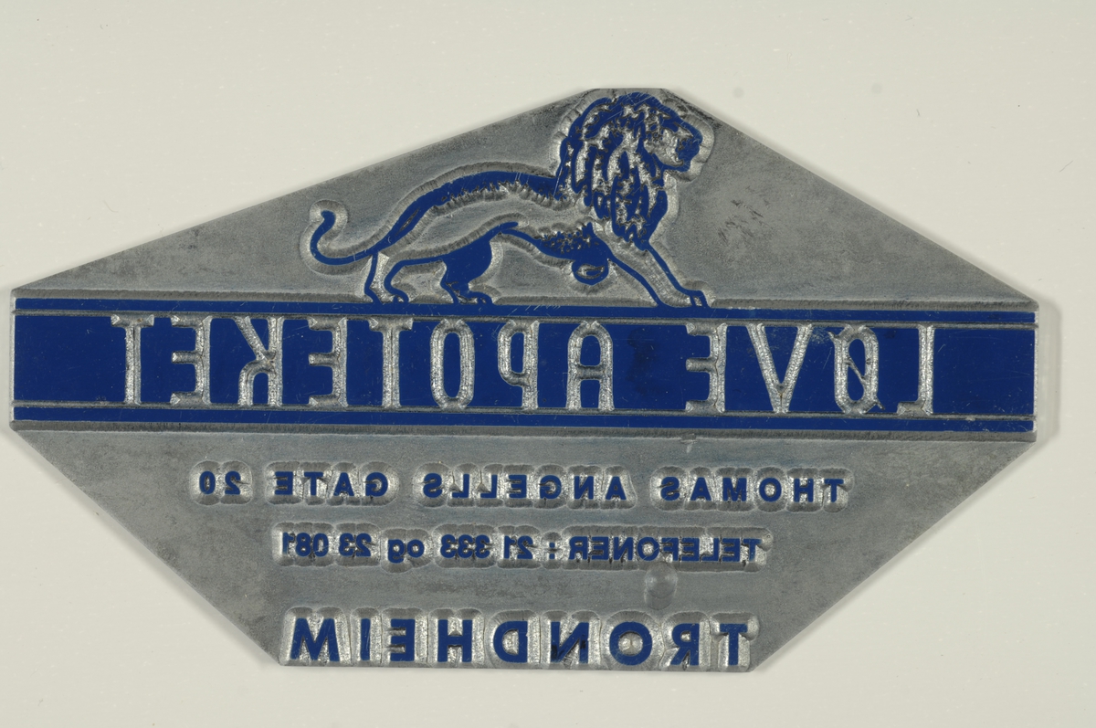 Usymetrisk åttekantet metallplate med tekst og løvesymbol i høytrykk, samt en skåret tekst.