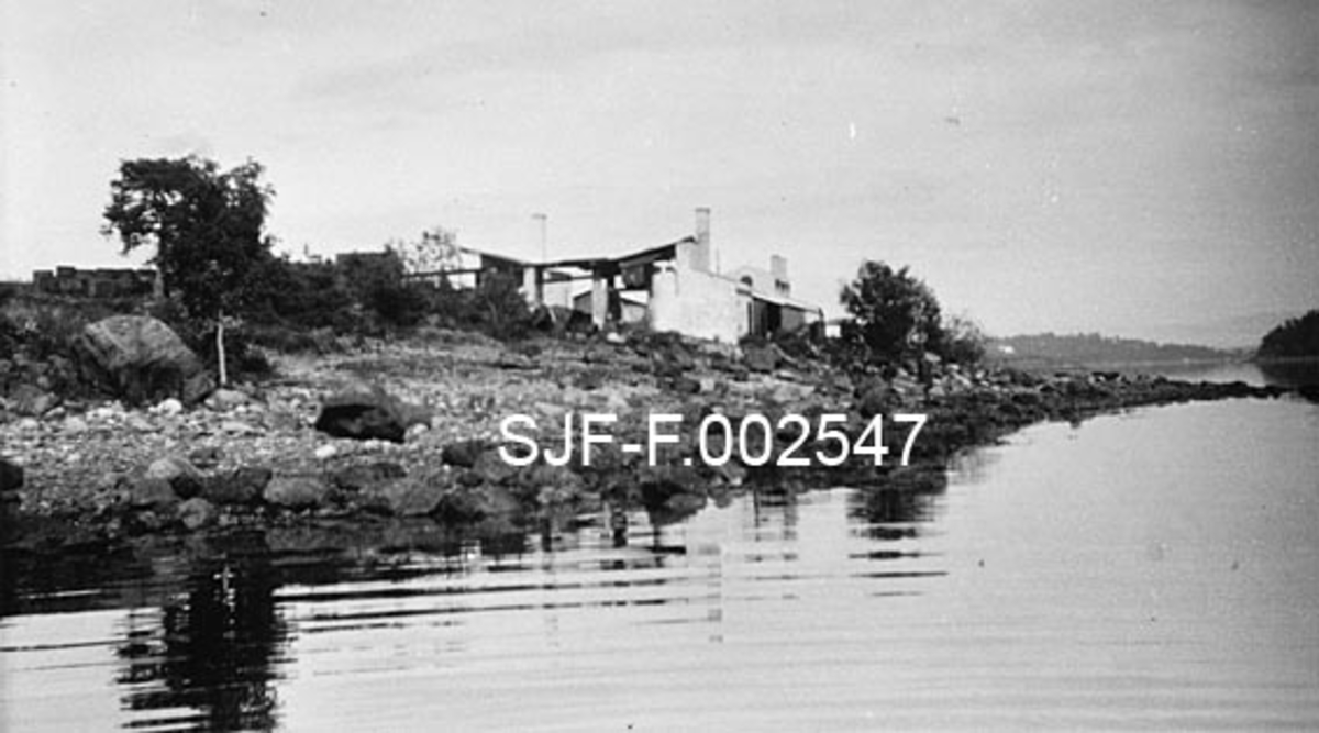Fabrikkanlegget til firmaet Schwencke & Co's Eftf. på Børsholmen i Asker, fotografert fra fjorden sommerstid.  Fotografiet er antakelig tatt forholdsvis kort tid etter at anlegget ble bygd, i 1924.  Bygningene danner silhuett mot den lettskyete himmelen.  Schwencke & Co. framstilte bek og andre tjærebaserte produkter på Børsholmen. 