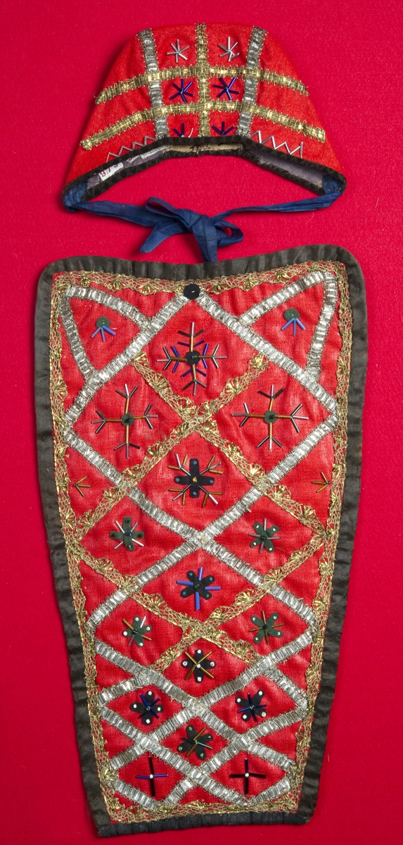 Rød kristnableie i ull med dekor av metallbånd, glassperler og klede.
