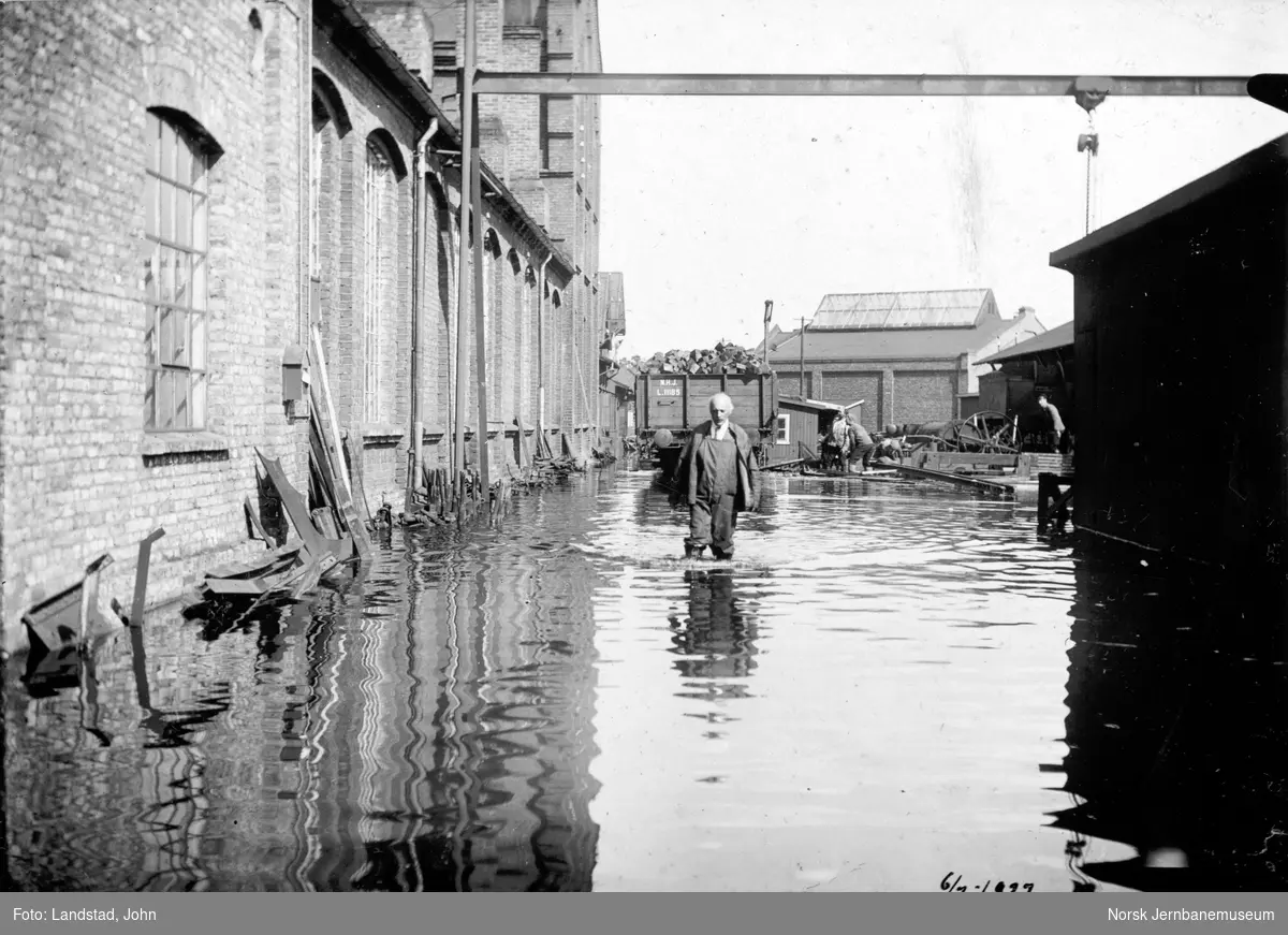 Flommen i 1927 : NSBs verksted Hamar, vannstand 8,10 meter, med fotografen, inspektør Landstad. Smie og maskinverksted til venstre
