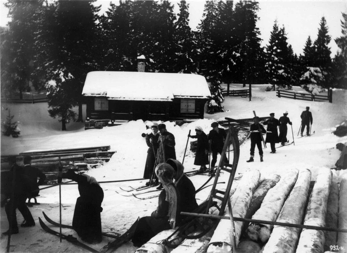 Frognerseteren, Oslo. 1908-1910. Skiløpere og akende. Tømmer. 
Hytte i bakgrunnen.