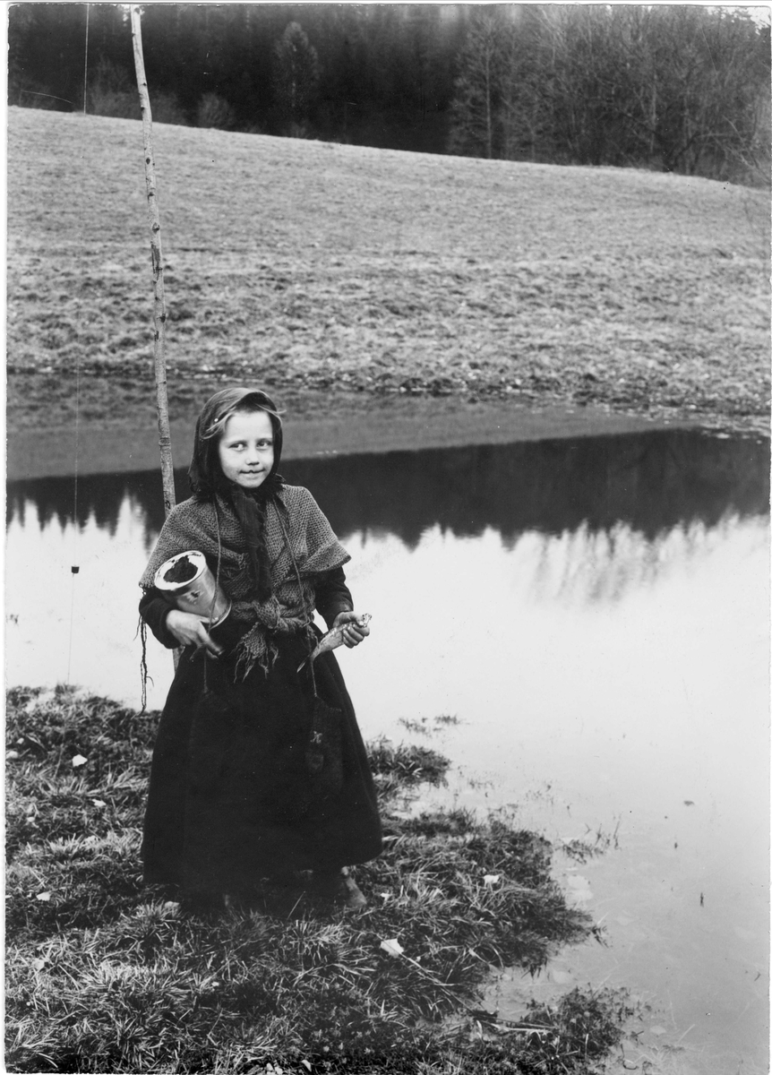 Pike med med fiskestang, fisk og blikkboks ved elv, ukjent sted.
Serie tatt av Robert Collett (1842-1913), amatørfotograf og professor i zoologi. 