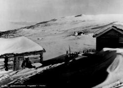 Avfotografert postkort. En mann sitter inntil tømmerveggen p