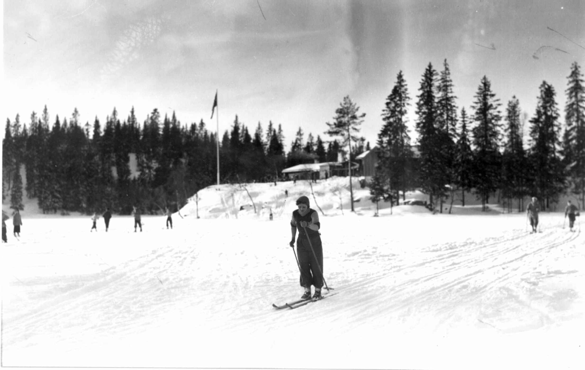 Skiløpere i Nordmarka, Oslo. 1934. Tryvannstua
med flagget til topps ses i bakgrunnen.   