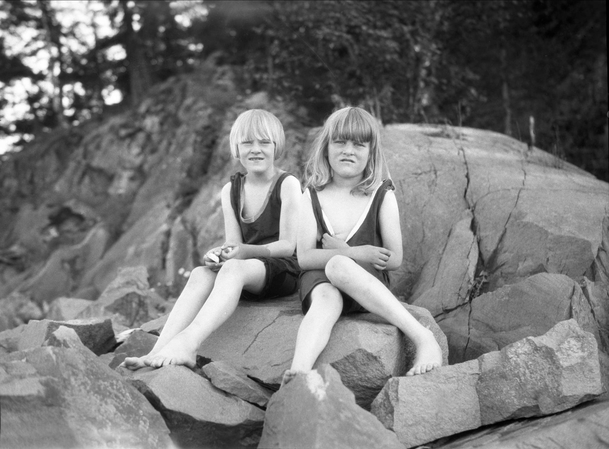 To jenter sitter i badedrakt på svarberg. Robsahm og Lund.