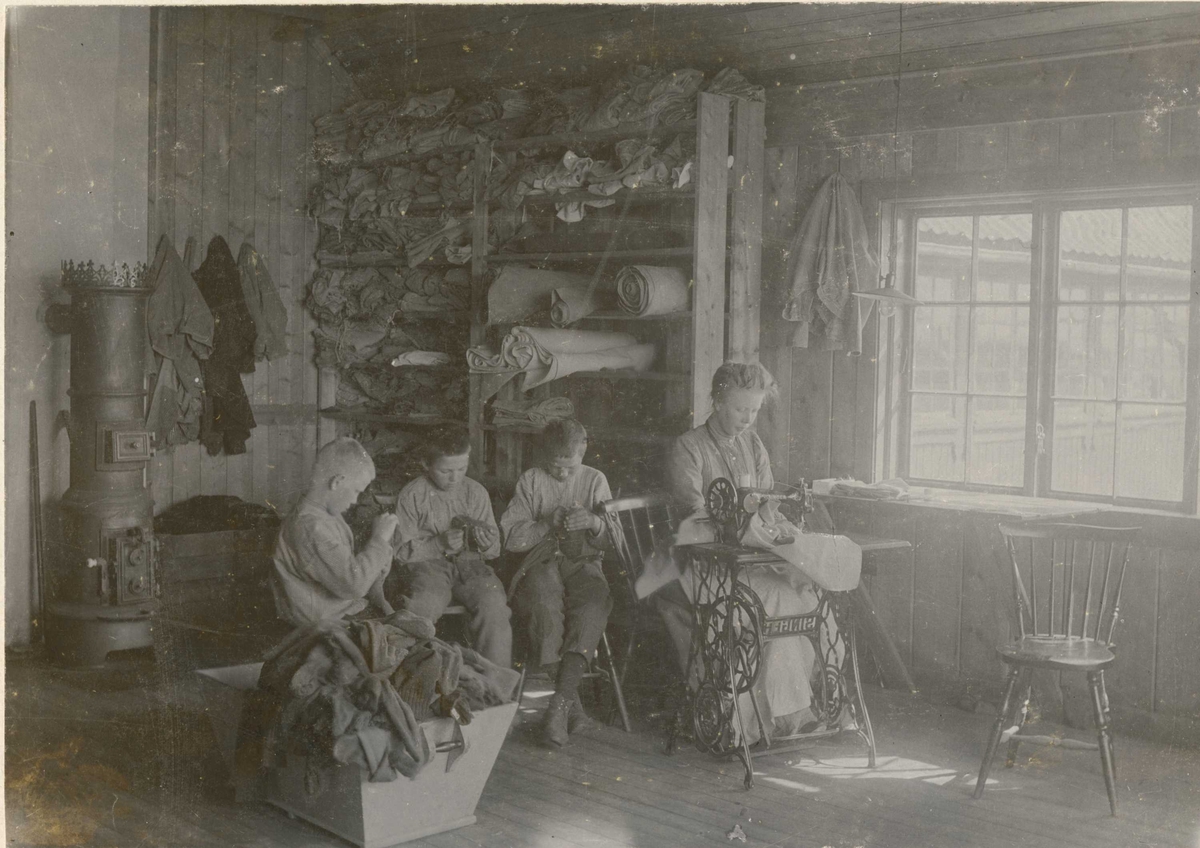 Skredderverkstedet på Bastøy skolehjem, Bastøya, Horten kommune, ca. 1903. Tre elever og en kvinnelig ansatt sitter og syr. 