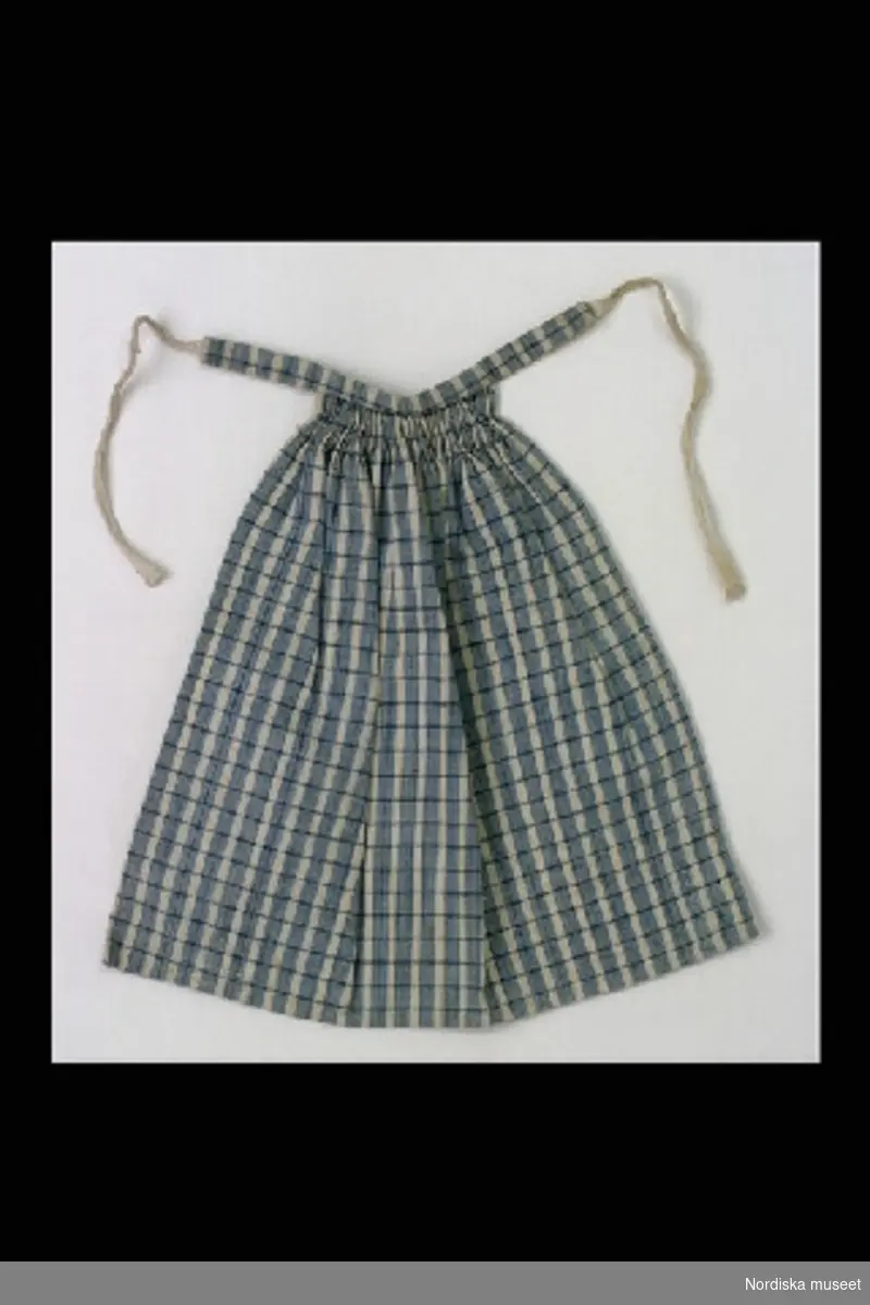 Inventering Sesam 1996-1999:
L 15,5 cm
Förkläde till docka, av bomull, ljusblå- och vitrutig, rynkad i midjan.
Bilaga
Helena Carlsson 1997
