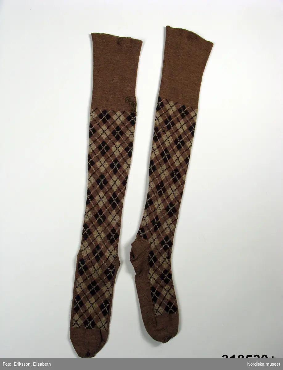 Golfstrumpor av tunnt ullgarn. Knälånga, benen golfrutiga i ljusbrunt, mörkbrunt och beige. Tillverkade omkring 1930.