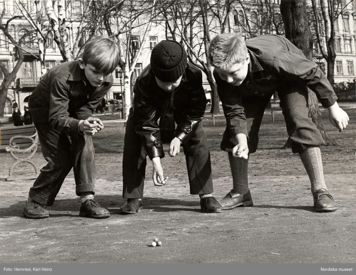 Tre pojkar spelar kula i park.