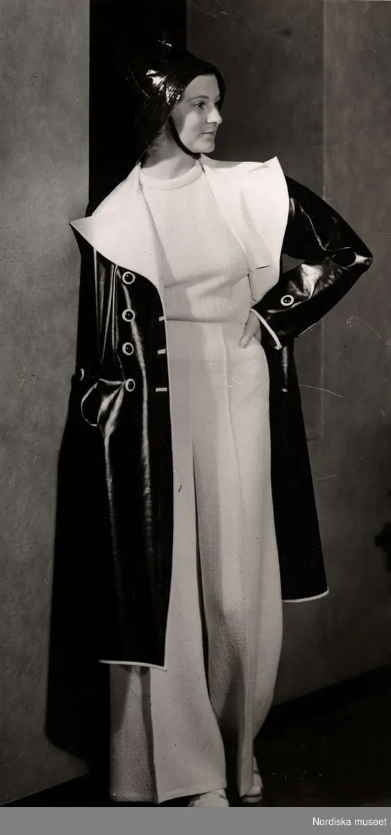 Dammode, en kvinnlig modell som är klädd i en vit tröja och byxor. Samt en svart regnkappa och regnhatt. Nordiska Kompaniet 1938.