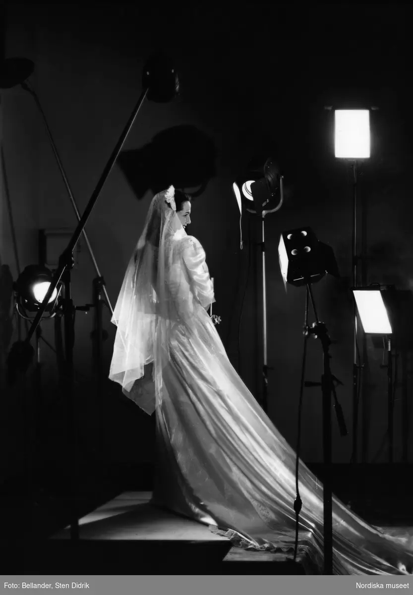 Modell klädd i brudklänning poserar för fotografering omgiven av blixtar i studio.