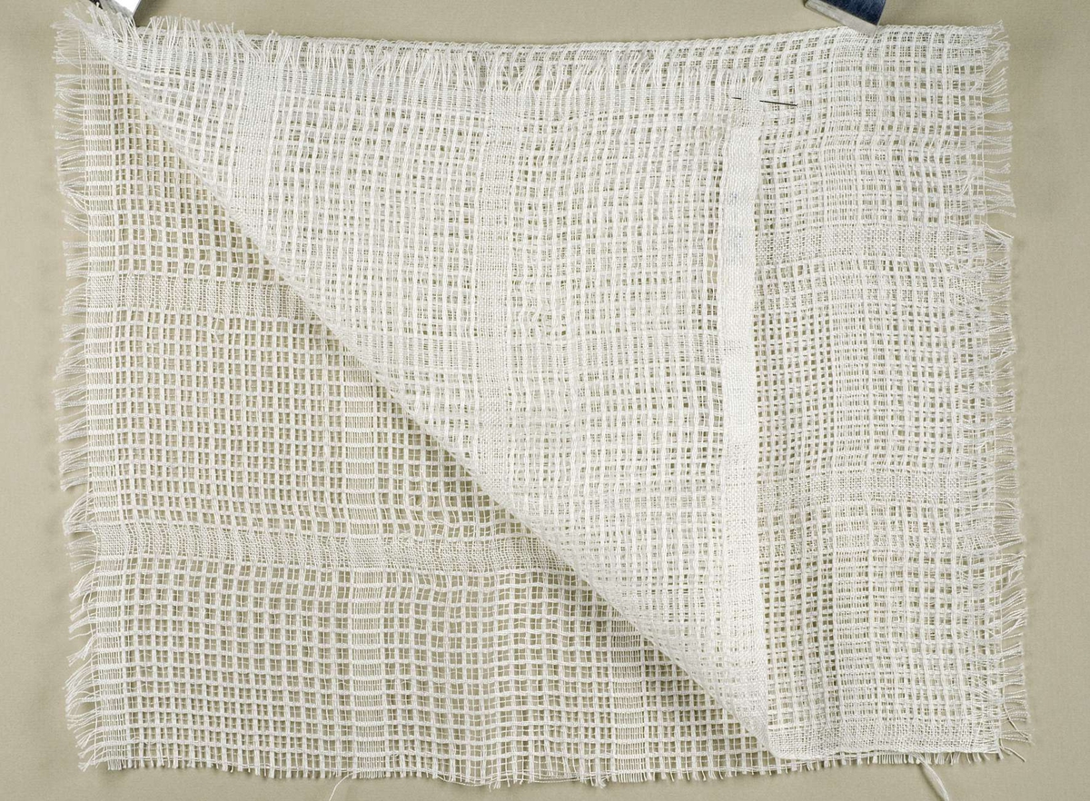 Vävprov av vitt gardintyg med vävt rutmönster. Vid vävprovet sitter en vit etikett med texten "Väv 229, Brev 315-316, 1959".