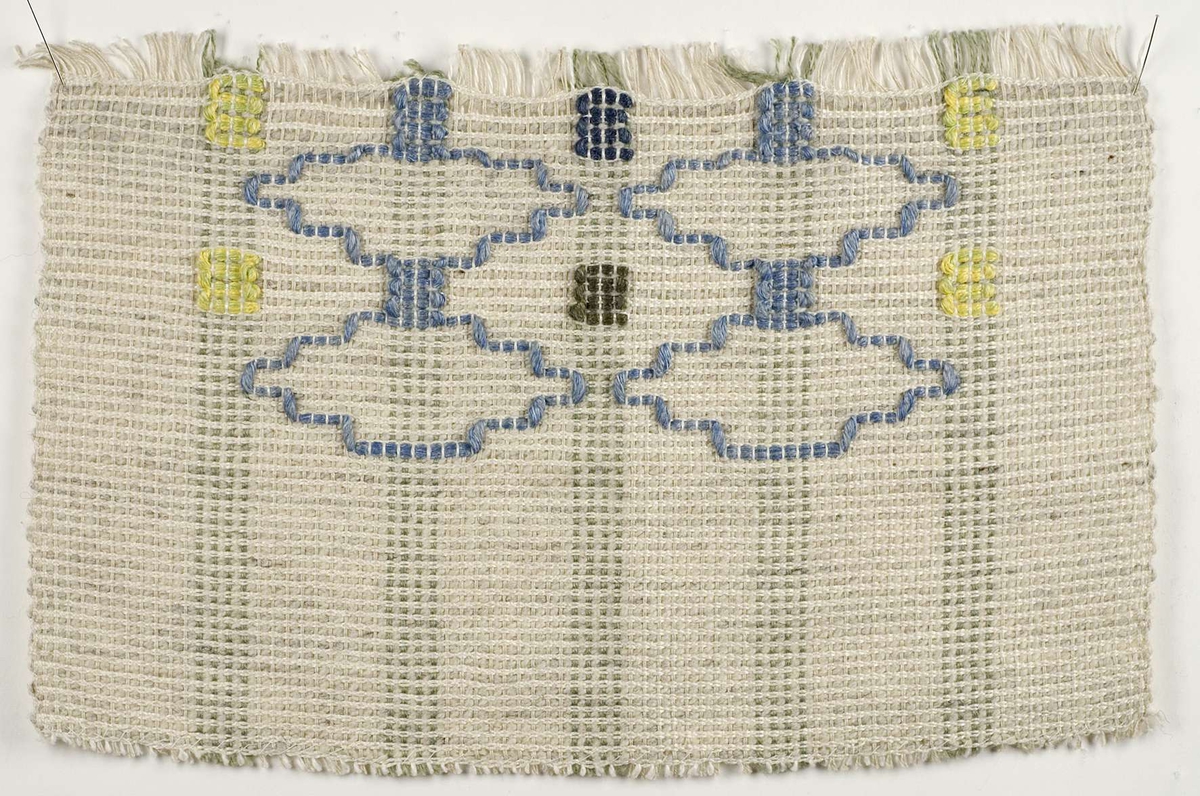 Vävprov av kuddtyg som är mönstrat med inplockat garn. Kuddtyget är i färgerna vitt, grått, gult, blått och grönt och det är vävt av lin och ull. Vävprovet är märkt B.2645.