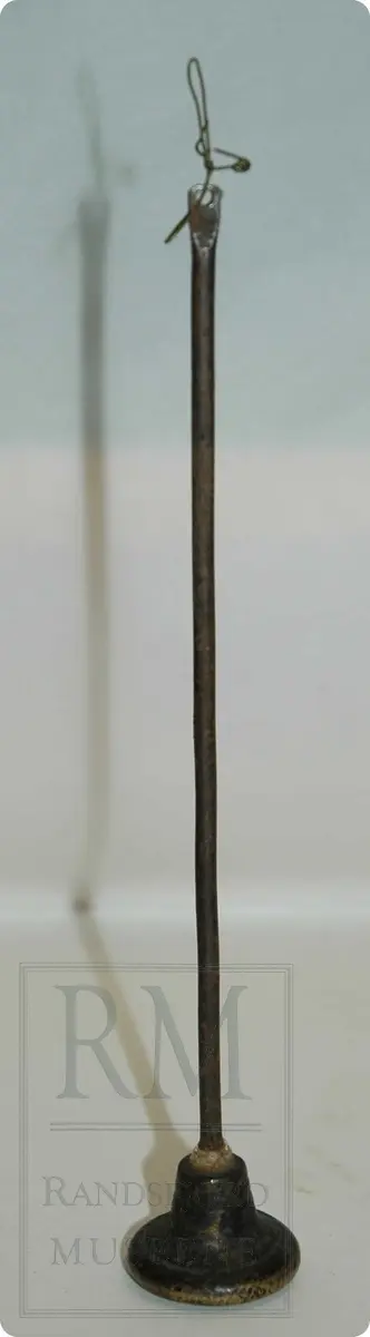 Bismervekt avjern. En avlang sylinderformet stav - med et lodd i den ene enden. Loddet er av messing. Staven har en krok av ståltråd festet i ene enden.