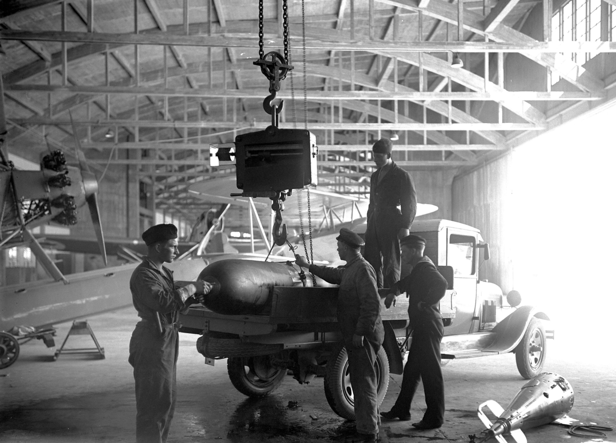 Arbete med torpeder för flygplan i hangar på F 2 Roslagens flygflottilj, 1932. Fyra personer i arbete med att lyfta av en torped från lastbil.