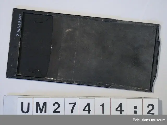 Fem svarta plåtkassetter för  filmexponering, H 6,2 x B 10 cm samt en fanerad träskassett med plats för två glasplåtar. H 30 x B 20,9 cm. Hör till kamera UM027413:1.