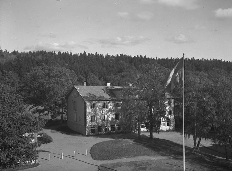 Text till bilden:"Skolanoch gårdsplanen är omgiven av barr och lövträd V.U.".