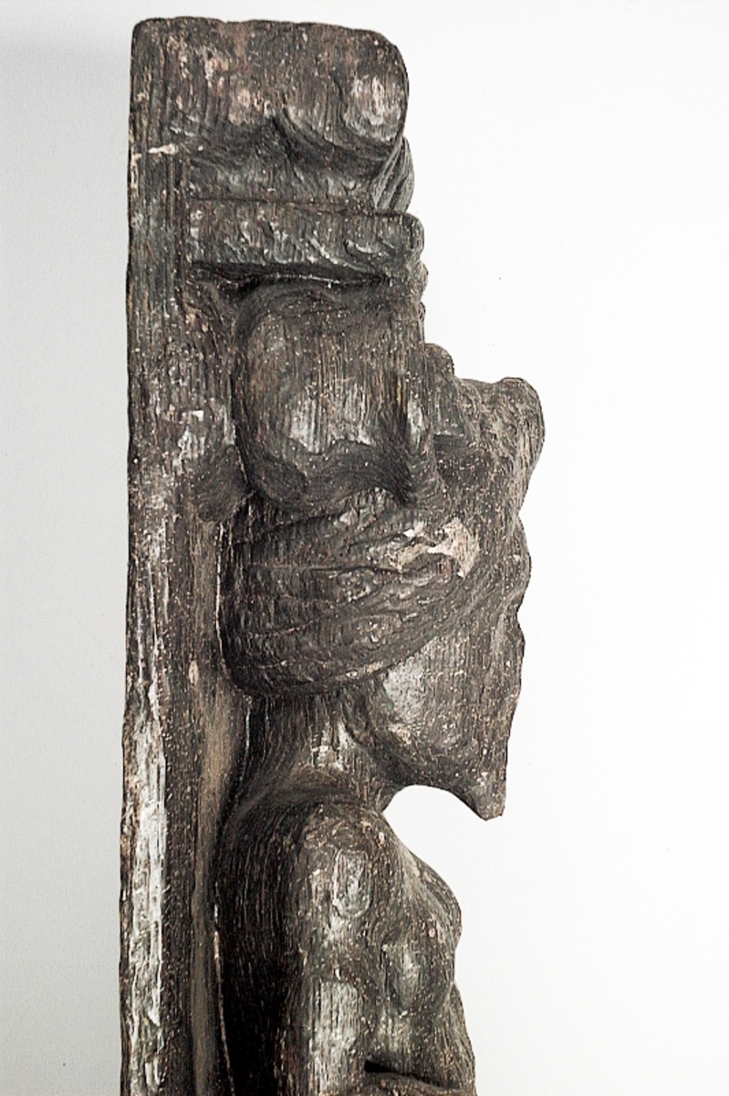 Skulpterad pilaster föreställande en skäggig, naken herm under joniskt kapitäl.

Hermen är iförd en stor turban. Huvudet är frontalställt. Vänster hand vilar på höften.

Nedtill är pilastern prydd med ett stort, bukigt och sköldliknande ornament samt blad- och rullverksbildningar. Längst ner syns en naken putto bärande en blomsterkorg på huvudet. Fotändan har formen av en tunn, snedskuren och slät tapp eller tunga som kan beskrivas som en fortsättning på bakstycket. Skulpturens baksidan är slät.

Skulpturen är relativt välbevarad, höger hand saknas dock.



Text in English: Sculpted pilaster with bearded naked Herm under an Ionic capital.

The Herm is wearing a large turban. The head is placed en face. The left hand rests on the hip.

The lower section of the pilaster is decorated with a large, bulging shield-like ornament and leaf and scroll-work formations. Below is a nude putto with a flower basket on its head. The foot end is shaped as a thin, smooth, angled tenon that may be described as an extension of the backboard. The rear side is smooth.

The sculpture is rather well preserved. The right hand is missing.