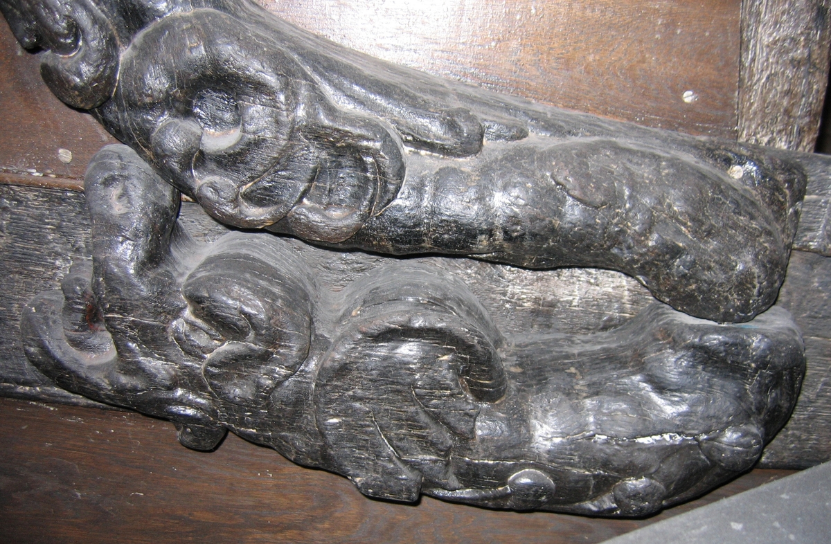 Skulpterad drake, återgiven i vänster profil.
Draken har vidöppen käft med kraftigt uppdragen nos, långt öra och rund drakvinge av fladdermustyp. Magen är prydd av bladslingor med förtjockade ändar. Stjärten med dess avslutande drakfena fortsätter uppåt och avtecknar sig längs stjärten till en triton, se fyndnummer 05943. Baksidan är slät.
Skulpturen är välbevarad, dock något ytsliten.

Text in English: Sculpture of a dragon in left profile.
The dragon is depicted with wide-open mouth, an up-turned nose, long ears and rounded dragon wings, like those of a bat. Its stomach is embellished with chains of leaves with thickened ends. Its hind end with terminating dragon fin extends upwards to be seen against a Triton''s rear, see No. 05943. The back is smooth.
The sculpture is well preserved if somewhat worn on the surface.