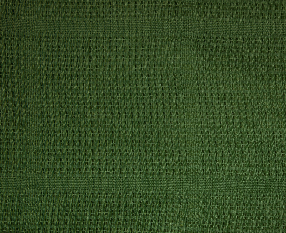 Överkast till säng. Tillverkat av handvävt linnetyg., mörkgrönt, vävt i stramaljbindning, myggtjäll med stora rutor. Två våder hopsydda på mitten, hörnen formade för att passa omstopp och nedhängande del fram. Sidorna, nedre kanten fram och den tänkta viklinjen för nerhänget kantade med gröna linneband. Överkastet är helfodrat med grönt linnetyg i tuskaft.