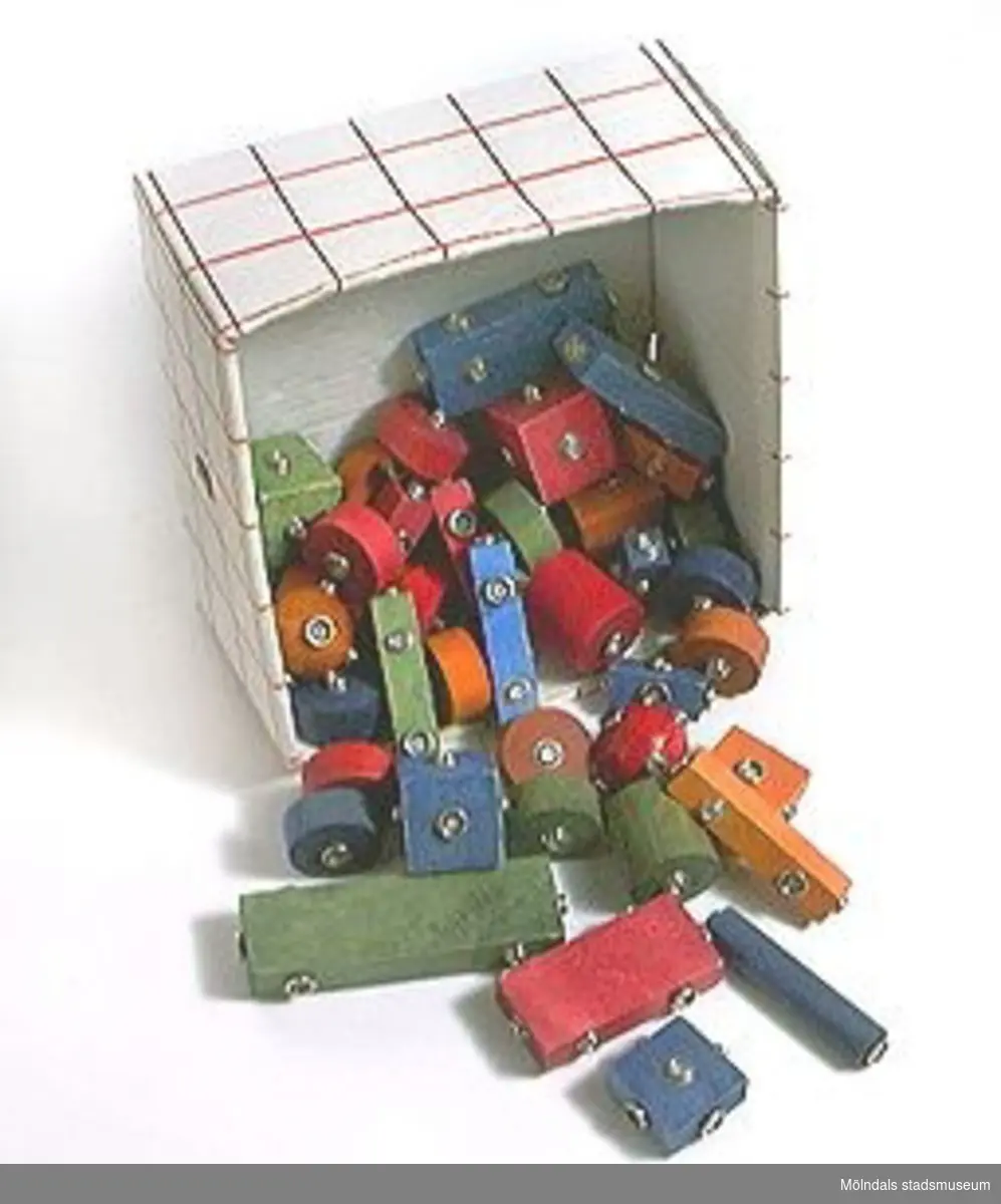 Byggklossar i 46 delar, så kallad Brio-Lego. Fästs ihop med knappar.Förvaras i en papplåda.