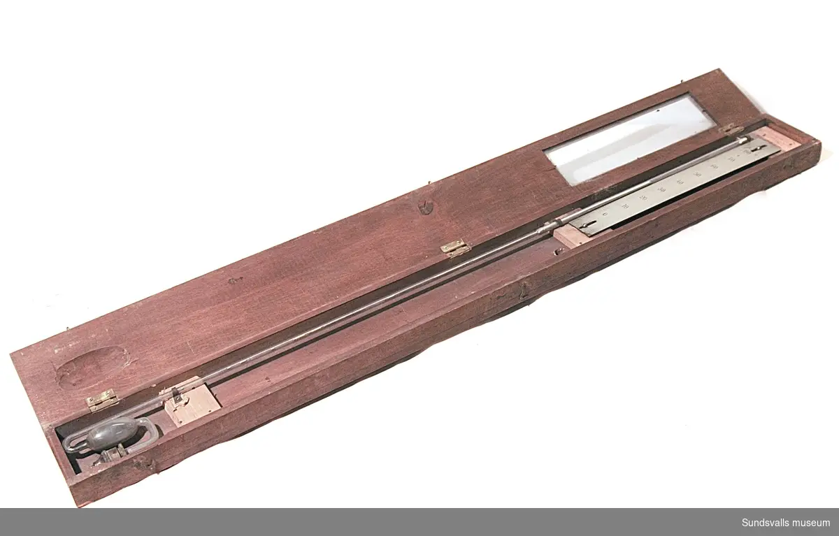 Mätinstrument. Instrumentet är inkapslat i ett smalt träskåp med dörr försedd med glasruta. Det utgörs av ett genomskinligt rör, vilket längst ner har en utbuktning, som rymmer kvicksilver. Innanför dörrens glasruta sitter en skala från 0 till 80. Enhet finns ej angivet.