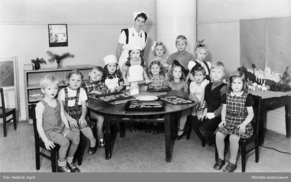 Bosgårdens barnträdgård 1938-1945. Fröken och barn som står uppställda bakom ett runt bord inför fotografering.