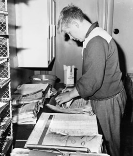 Brevbärarebiträdet Anders Håkansson fördelar postabbonerade tidningar efter utdelningslista.  Postexpeditionen i Åkersberga, augusti 1961.