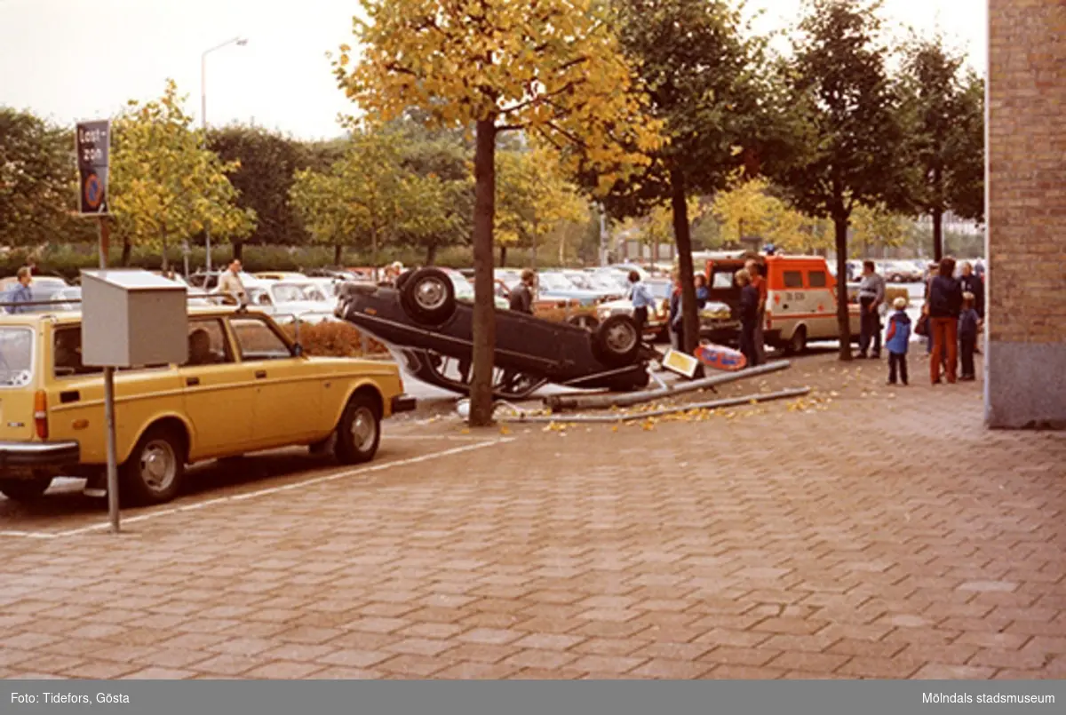 En bil ligger upp-och-ner-vänd, 1970-tal. Människor ser på när ambulanspersonal arbetar.