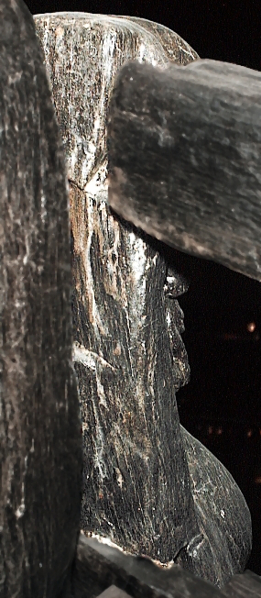 Skulptur av en triton, svängd mot höger.
Tritonen är framställd i vänster profil och avtecknar sig i hög relief mot det släta bakstycket. Tritonen har en stor näsa och treflikig mustasch. På huvudet sitter en hjälm med dekorativa bladvoluter. Armarna är ersatta av långa, flikiga bladslingor. Bålens övergång i den fjällförsedda fiskstjärten markeras av stora bladbildningar. Tritonens stjärt döljs bakom stjärten och vingen till en under liggande drake, se fyndnummer 21277. På baksidan finns urtag för relingslisten.
Skulpturen är mycket välbevarad.

Text in English: A sculpture of a Triton curved to the right.
The figure is seen in left profile, in high relief against a plain back board. The face has a large nose and a moustache that splits into three parts. On its head is a helmet with decorative leaf volutes. The arms are replaced by long, lobed leaf formations. The transition area between the male torso and the scaled fish-tail is decorated with large leaves. The rear is hidden behind a dragon''s coiled tail and broad wing situated below, see No. 21277. There are notches on the back that fit into the railing.
The sculpture is very well preserved.