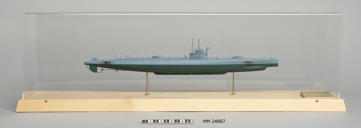 Ubåtsmodell Hvalen i monter. Modell av alträ med detaljer av mässing, målad med cellulosafärg. Grått skrov. Monter av plexiglas på träplatta. Mässingsbricka i montern med uppgifter om modellen.
