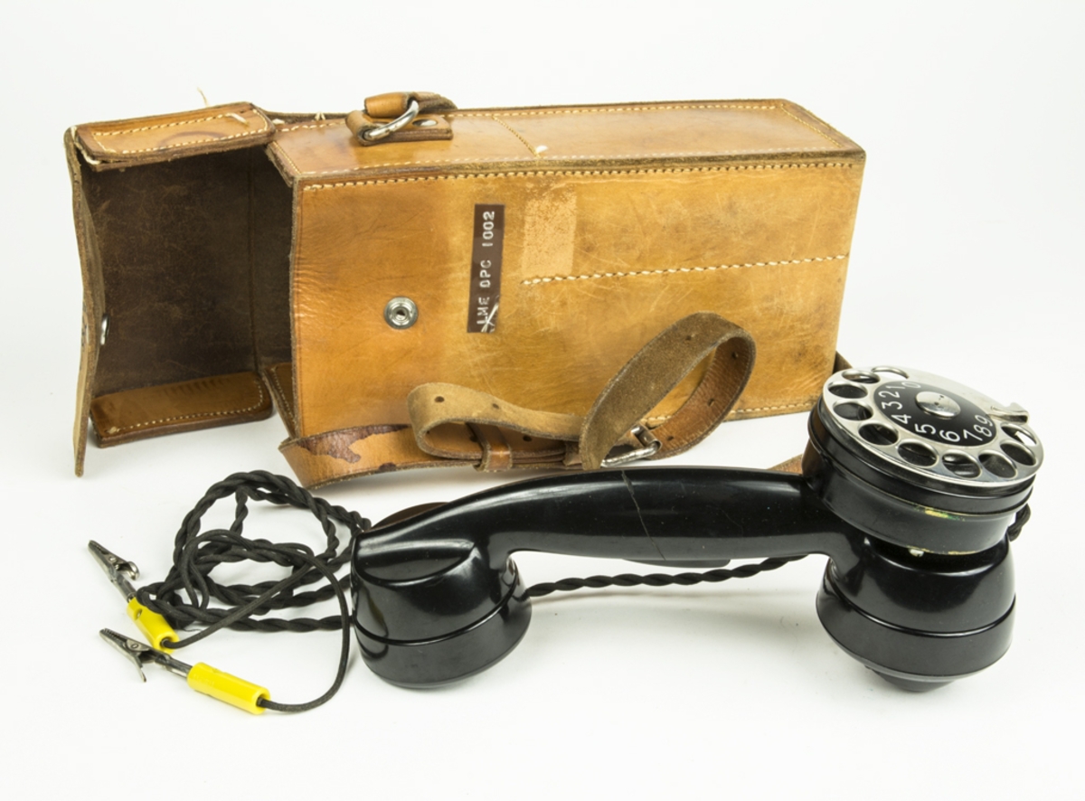 Fälttelefonen består av en svart telefonlur med siffersnurra på. Till telefonen är två kablar med gula krokodilklämmor fäst, klämmorna användes till att koppla sig mot telefonledningarna. Finns en till förvaringslucka i läderväskan men denna är emellertid tom.