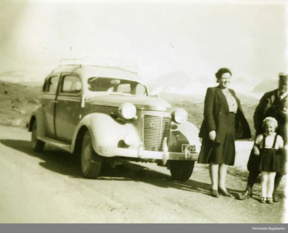 Frå venstre: Kristi og Knut Langehaug, frå Søre Fossheim på Ullsåk i Hemsedal. Framfor Knut står dottera Kirsten. Drosje F 12317  Bilen er ein Chrysler 1937 mod.