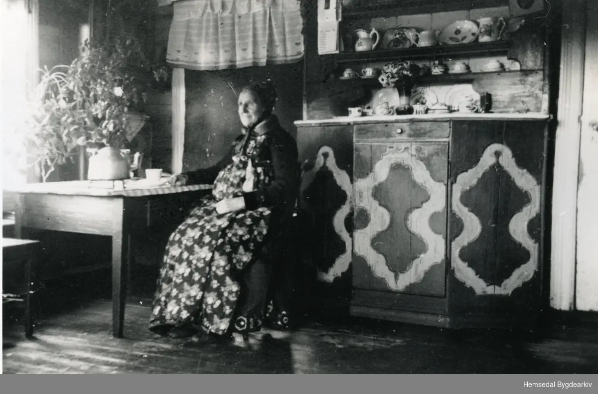 Birgit Nilsongard (1865-1955) sit i stova framfor Framskåpet i kyrkjeklede.
Biletet er teke ca. 1930.