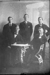 Reproduksjon av tre menn som står bak to som sitter.