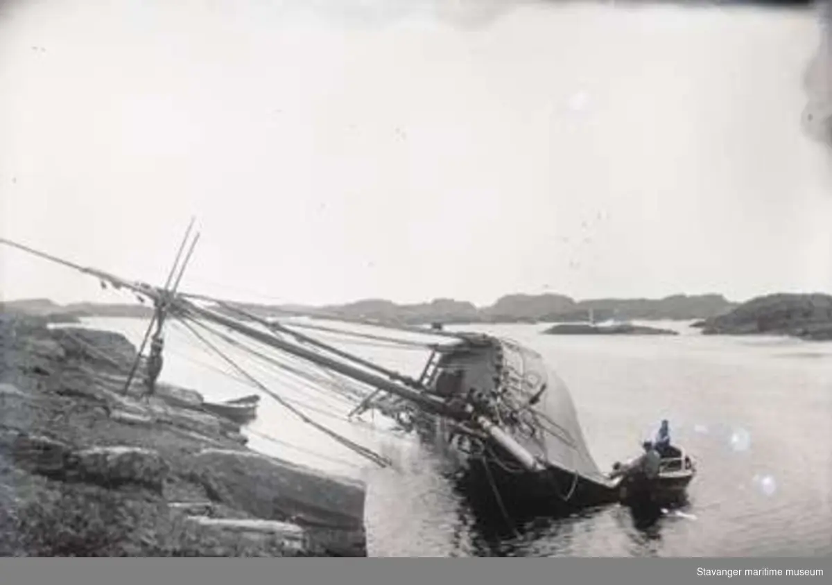 To menn i robåt kjølhaler et seilskip. Fotografiet er tatt ved Haganes, sett mot øst.