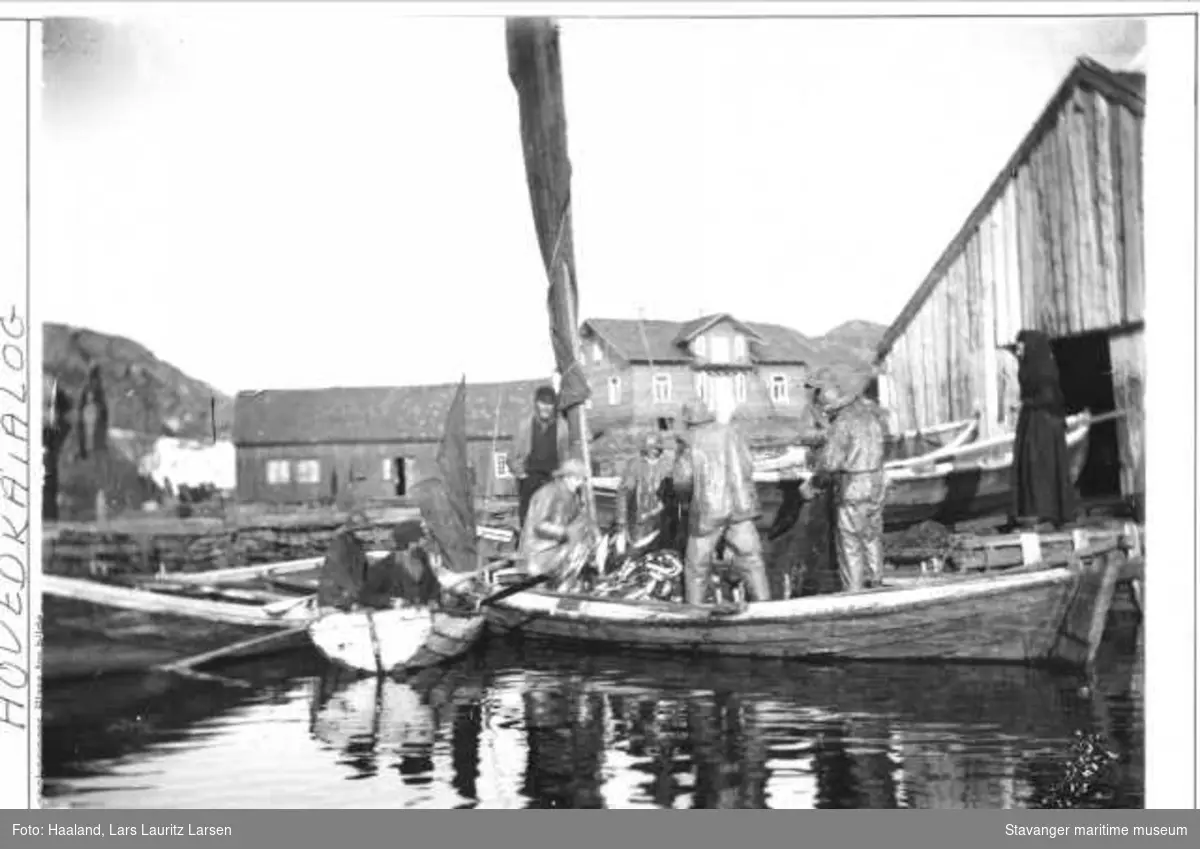 Fiskere som har kommet inn til Ydstebøhavn med sild. Lauritz Haalands villa ligger midt i bildet til høyre, det er under bygning. Bildet er tatt ca 1885. 