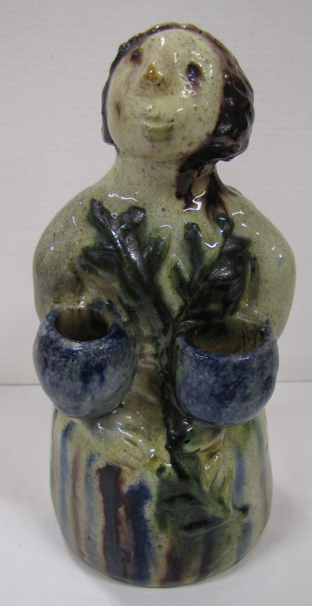 Keramikfigur med vingar på ryggen och två ljushållare vid armarna.

Se bilaga VM 18 804