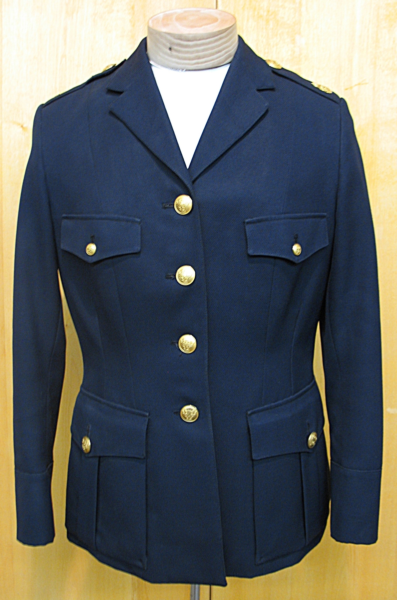 Kvinlig polisuniform med kjol (19 150b). Inköpt slutet av 1960-talet. Kjol till uniform slutade att användas omkr. 1975.

Jackan har 4 utanpåfickor och blanka knappar.