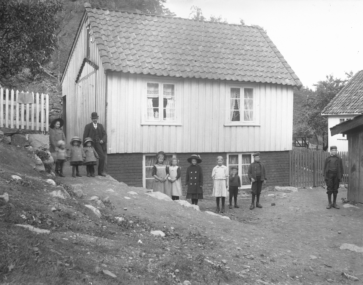 Lite hus med voksen mann og mange barn utenfor - på Bakken(?) Kragerø
