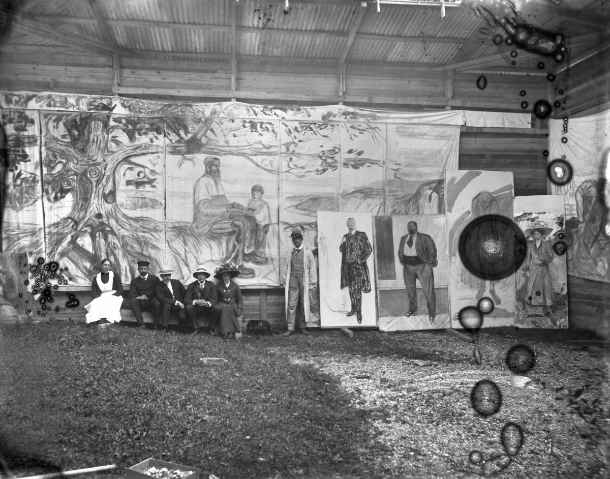 Fra E. Munchs friluftsatelier på Skrubben, flere malerier, kunstneren stående, to kvinner og tre menn sittende