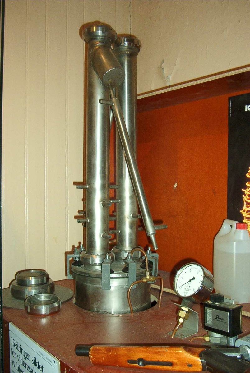 Stort HB-apparat. Tanken er innebygd i en kasse av kryssfinér og hengslett lokk. På instrumentene som hører med står det: Bergs Maskin, Trondheim kp/cm2, Ranco, Trade mark registered, Penn. En stor sikring og en bryter 0-1-2. 3 kanner med "sprit".
