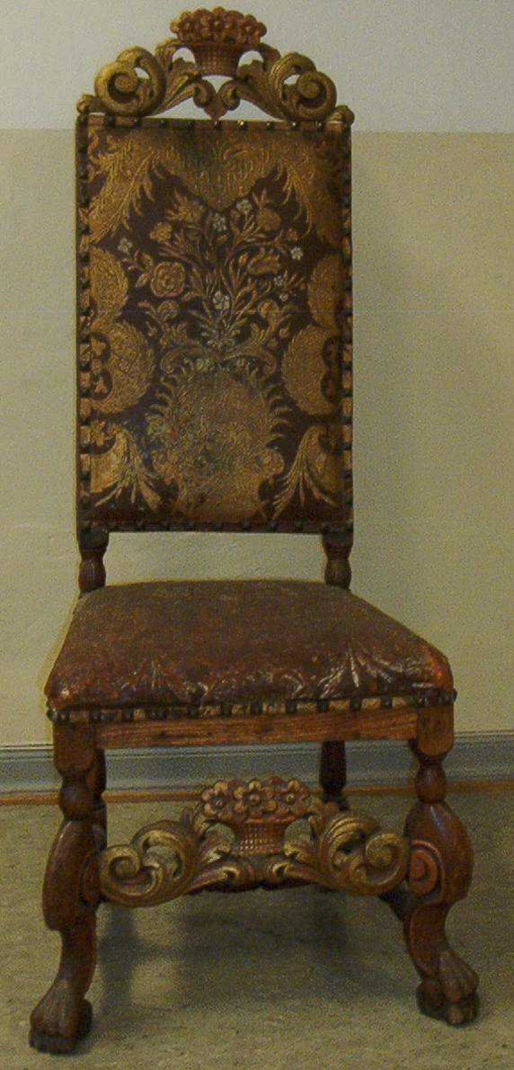 Barokkstol i tre, en såkalt Trondhjemsstol med høy rygg, fra tidlig 1700-tall. Stolen er rikt utsmykket med utskjeringer og maling i forskjellige farger. Både ryggen og setet er trukket med gyldenlær.
