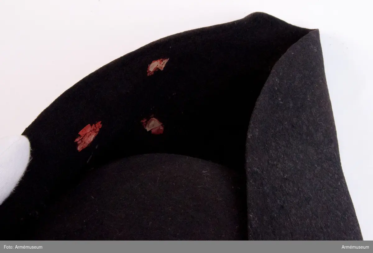 Trekantig svart hatt med mässingsknapp och rester av rött lacksigill.