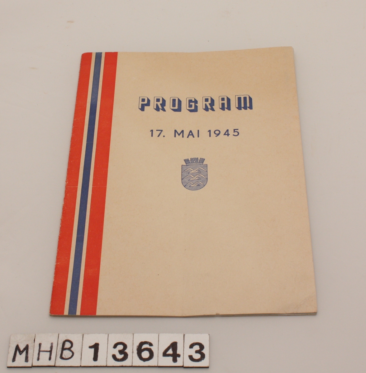 Rektangulært program for 17. mai 1945. På forsiden er til venstre et langt bånd i det norske flaggets farger. Under tittel er Haugesund kommunevåpen. Heftet inneholder program og sanger.