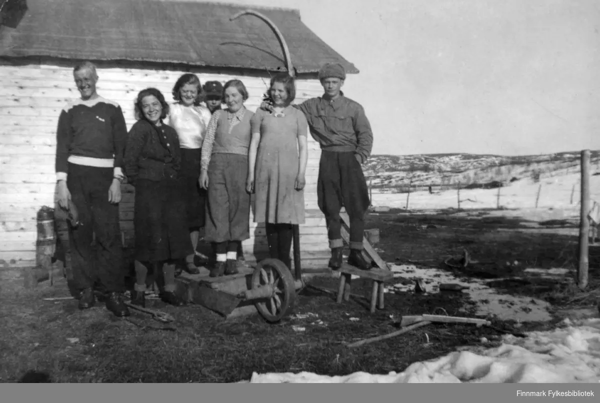 Gruppebilde tatt på gården Veines i Øvre Neiden, ca. 1938. Mannen til venstre er så høy at flere av de andre har klatret opp på krakker o.a. for å komme opp i tilnærmet hans høyde